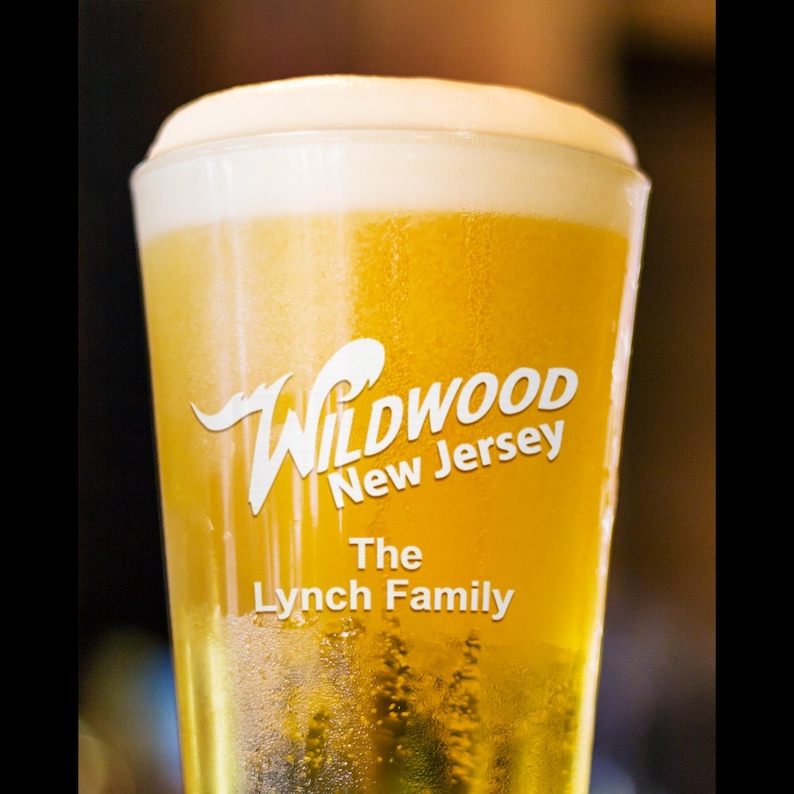 May include: A tall glass of beer with a white head. The glass has a logo that says "Wildwood New Jersey The Lynch Family".