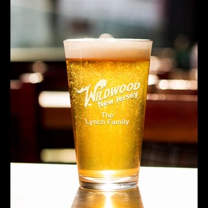 May include: A clear glass pint glass filled with a golden yellow beer. The glass has the text "Wildwood New Jersey The Lynch Family" etched on the side.