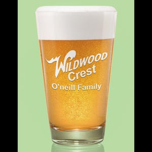 Peut inclure: Un verre &agrave; bi&egrave;re transparent rempli de bi&egrave;re et surmont&eacute; d'une mousse blanche. Le verre porte l'inscription blanche "Wildwood Crest" et "O'Neill Family". La bi&egrave;re est de couleur dor&eacute;e.