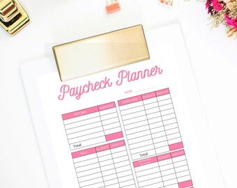 Op de afbeelding: Een printbare loonstrookplanner met roze koppen en zwarte lijnen. De planner ligt op een wit oppervlak met gouden clips en een gouden nietmachine.