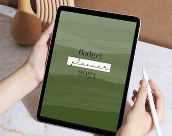 Op de afbeelding: Een digitale tablet met een groene aquarel achtergrond en de tekst "Budget planner 2023" op het scherm. Een persoon houdt de tablet vast en gebruikt een stylus.