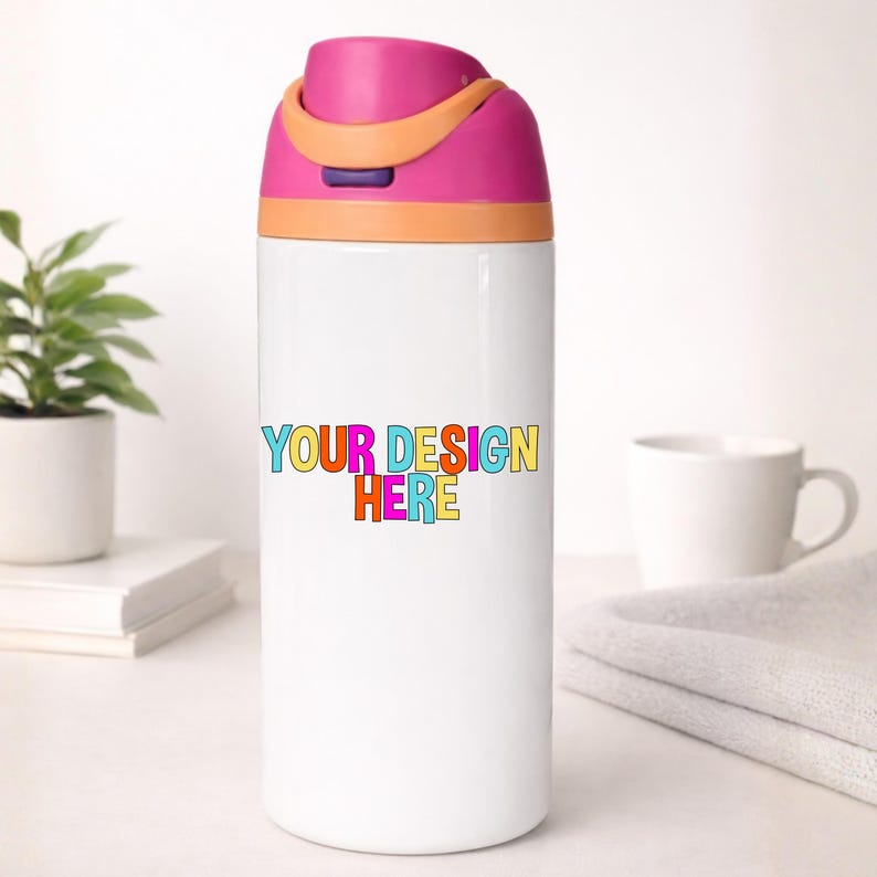 May include: White water bottle with a pink and orange lid. The bottle has the text "YOUR DESIGN HERE" in colorful letters. A small plant, a white mug, and a folded towel are in the background.