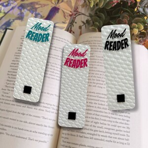 May include: Three white bookmarks with the text "Mood Reader" in different colors: teal, pink, and black. The bookmarks have a textured surface.