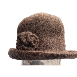 May include: A brown cloche hat with a decorative flower on the side. The hat has a rounded crown and a small brim. The hat is made of a textured, wool-like material.