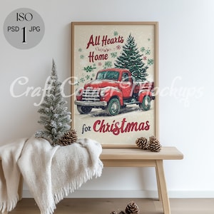 May include: A framed print with a vintage red truck and Christmas tree illustration. The text reads "All Hearts Home for Christmas." The print is displayed on a wooden bench with a small Christmas tree and a cream-colored blanket.