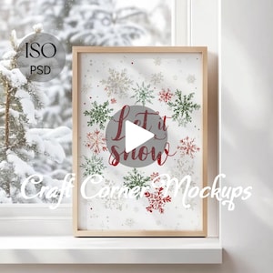 May include: A framed print with a winter theme. The artwork features the phrase "Let it snow" in red script within a gray circle, surrounded by red, green, and white snowflakes. The frame is made of light-colored wood.