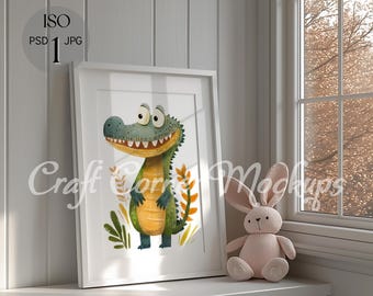 May include: A white framed print of a cartoon crocodile with a toothy grin, surrounded by green and yellow leaves. The print is hanging on a white wall next to a window with a view of trees. A pink stuffed bunny sits on a white shelf below the print.