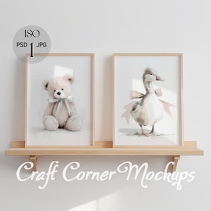 Puede incluir: Dos impresiones en acuarela enmarcadas en una estantería de madera. Una impresión presenta un oso de peluche con un lazo, la otra un pato con un lazo. Las impresiones son en colores pastel claros, creando una estética suave con temática de guardería.