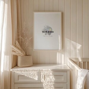 May include: A framed white poster with the text "YOUR DESIGN A1-A4 Craft Corner Mockup" hangs on a cream-colored wall. A woven basket with dried plants sits on a matching cream-colored dresser. A crib is visible in the background.