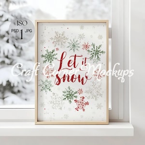 May include: A framed print with the words "Let it snow" in red script, surrounded by green, red, and gray snowflakes. The print is in a light wood frame and is displayed on a white windowsill.