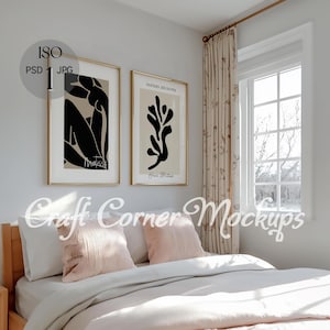 May include: A bedroom interior with a white bed, two pink pillows, and a wooden headboard. Two framed black and white art prints hang on the wall above the bed. A window with white blinds is visible in the background.
