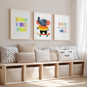 May include: Three framed wall art prints featuring a colorful elephant on a skateboard and the text Good Vibes Only and Start each day with a Smile, displayed above a light wood storage bench with five beige fabric bins and decorative pillows.