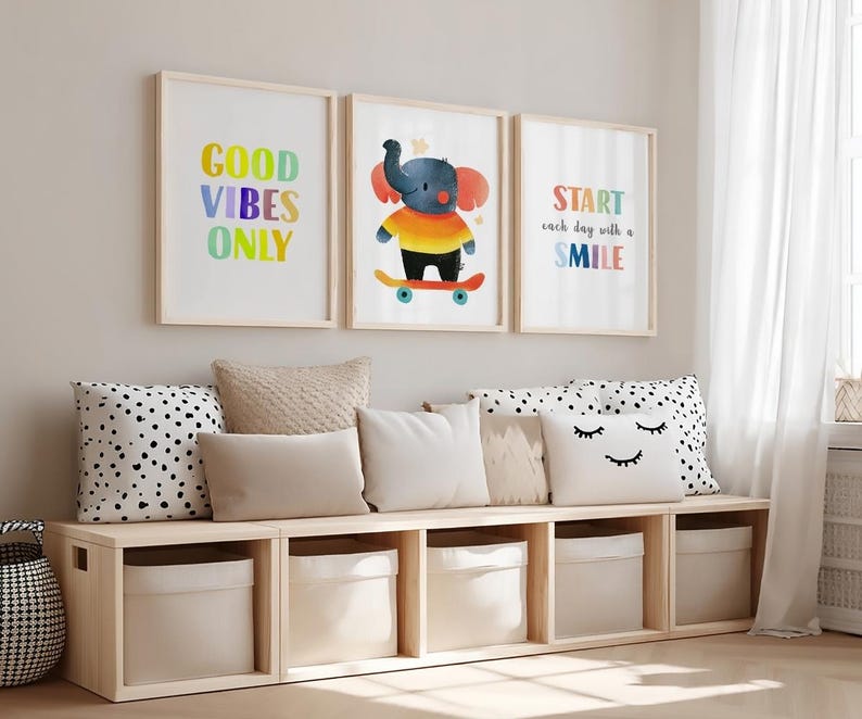 May include: Three framed wall art prints featuring a colorful elephant on a skateboard and the text Good Vibes Only and Start each day with a Smile, displayed above a light wood storage bench with five beige fabric bins and decorative pillows.