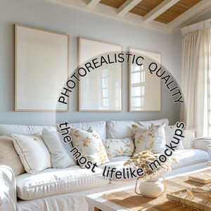 May include: A white couch with pillows in a living room with white walls and a wooden ceiling. There are three framed pictures on the wall behind the couch. The couch is decorated with throw pillows and a vase of dried flowers.