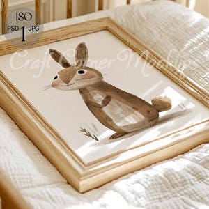 Puede incluir: Una ilustración enmarcada de un conejo marrón sobre un fondo blanco. El conejo está de pie sobre sus patas traseras con las patas delanteras levantadas. El marco es de madera clara.