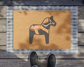 May include: A brown doormat with a white border and a black and orange Dala horse design.