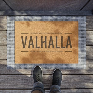 May include: A brown doormat with the text "In the thralls of a fighting heart, forever" and "VALHALLA" in black lettering. The text "In the thralls of a fighting heart, forever" is repeated at the bottom of the doormat.