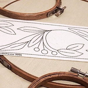 Op de afbeelding: Een witte stoffen strook met een zwart lijnpatroon van bladeren en bessen, voorzien van de tekst "Milan 8cm • BB049Mi 8cm • © The Haberdashess 2026". Twee ronde houten borduurringen met metalen spanschroeven liggen in de buurt.