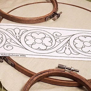 Op de afbeelding: Twee ronde houten borduurringen op een beige stof. Een lange witte strook stof met een herhalend zwart lijnpatroon van bloemen en de tekst "Florence 8cm • BB047FI 8cm • © The Haberdashess 2026" ligt over de borduurringen heen.