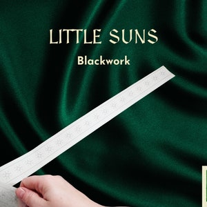 May include: A white fabric strip with a repeating pattern of small stars, labelled "Little Suns Blackwork". The fabric strip is being held by a hand against a dark green background.