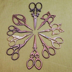 Può includere: Una collezione di forbici decorative in vari design e colori, disposte in un motivo circolare su una superficie verde. Le forbici presentano manici ornati e lame affilate, con colori che vanno dal bronzo all'argento.