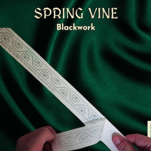 Op de afbeelding: Een witte strook stof met een zwartwerkontwerp van een wijnstok met bladeren. De tekst "SPRING VINE Blackwork Blossom Vine © 2013 The Haberdashurces. For personal use only" is gedrukt op de strook stof.