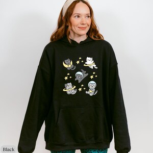 Peut inclure: Sweat &agrave; capuche noir avec un motif fantaisiste de chats de dessin anim&eacute; dans l'espace, des lunes et des &eacute;toiles. Le motif est en gris, jaune et blanc. Le sweat &agrave; capuche a une capuche &agrave; cordon et une poche kangourou.