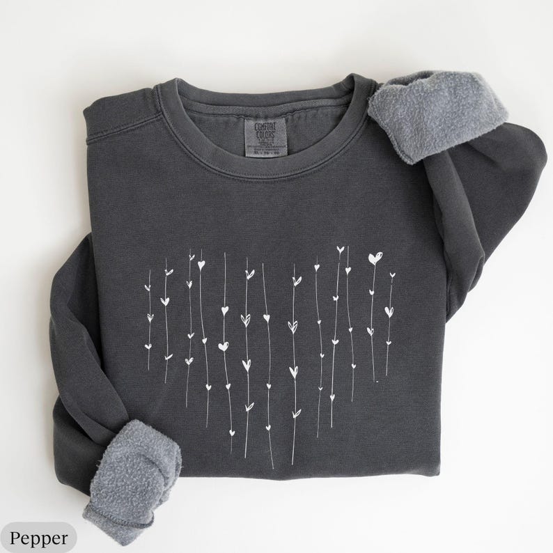 May include: A dark gray sweatshirt with a white heart design made of lines and small hearts. The sweatshirt has a crew neck and long sleeves.