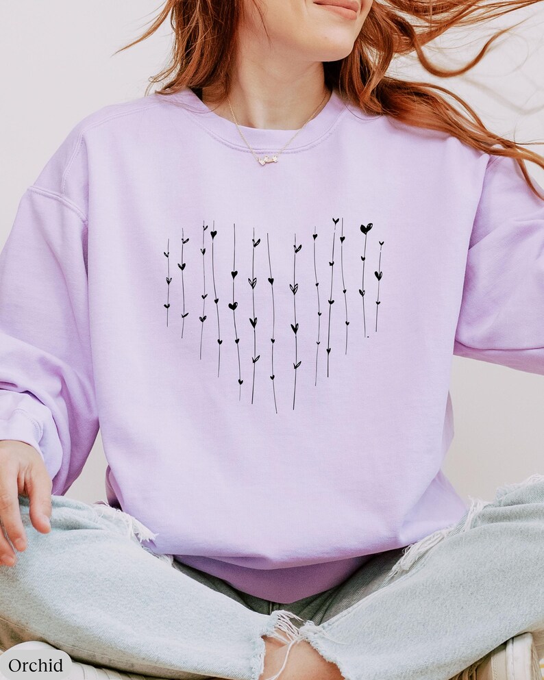 May include: A lavender sweatshirt with a black heart design made of small hearts and lines. The sweatshirt is a crew neck style.