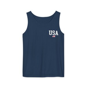 May include: Navy blue tank top with the word "USA" in white block letters and a small American flag graphic. The sleeveless shirt is made of a soft material.