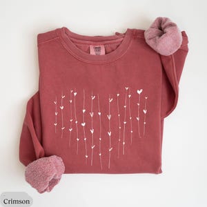 May include: Crimson red sweatshirt with a white heart design made of small hearts and lines. The sweatshirt is made of a soft, comfortable material.
