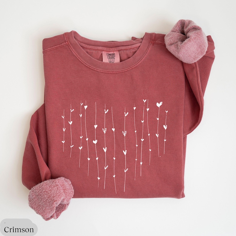 May include: Crimson red sweatshirt with a white heart design made of small hearts and lines. The sweatshirt is made of a soft, comfortable material.
