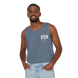 May include: A blue tank top with the word "USA" printed in white, along with a small American flag graphic. The tank top is a solid color and has a classic, casual style.