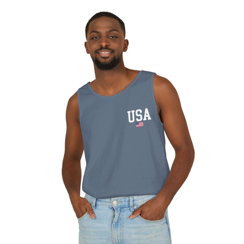 May include: A blue tank top with the word "USA" printed in white, along with a small American flag graphic. The tank top is a solid color and has a classic, casual style.