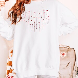 May include: White oversized sweatshirt with a red heart design made of small hearts and lines. The sweatshirt is shown on a model wearing it with grey shorts.