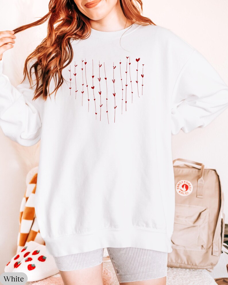 May include: White oversized sweatshirt with a red heart design made of small hearts and lines. The sweatshirt is shown on a model wearing it with grey shorts.