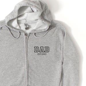 May include: Gray zippered hoodie with a black print that says "DAD EST. 2023".