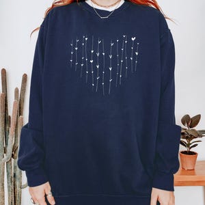 May include: A navy blue sweatshirt with a white heart design made of small hearts and lines. The sweatshirt has long sleeves and a crew neck.