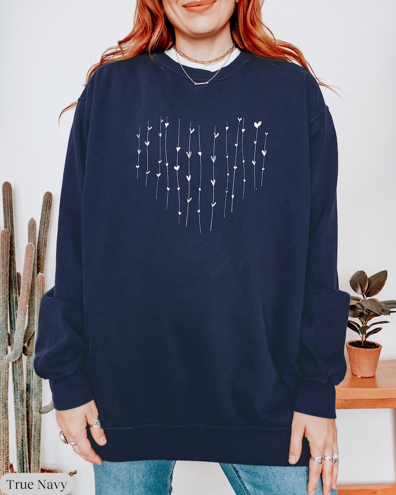 May include: A navy blue sweatshirt with a white heart design made of small hearts and lines. The sweatshirt has long sleeves and a crew neck.