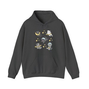 Peut inclure: Sweat &agrave; capuche gris fonc&eacute; avec une poche avant. Le sweat-shirt pr&eacute;sente un motif de chats de dessins anim&eacute;s en combinaisons spatiales et des &eacute;l&eacute;ments c&eacute;lestes comme des lunes et des &eacute;toiles. Les chats sont dans diverses poses, cr&eacute;ant un design ludique.