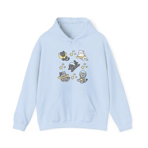 Peut inclure: Un sweat &agrave; capuche bleu clair orn&eacute; d'un motif ludique de chats de dessin anim&eacute; en combinaisons spatiales flottant dans l'espace. Les chats sont entour&eacute;s d'&eacute;toiles et de plan&egrave;tes. Le sweat &agrave; capuche a une poche avant et une capuche &agrave; cordon.