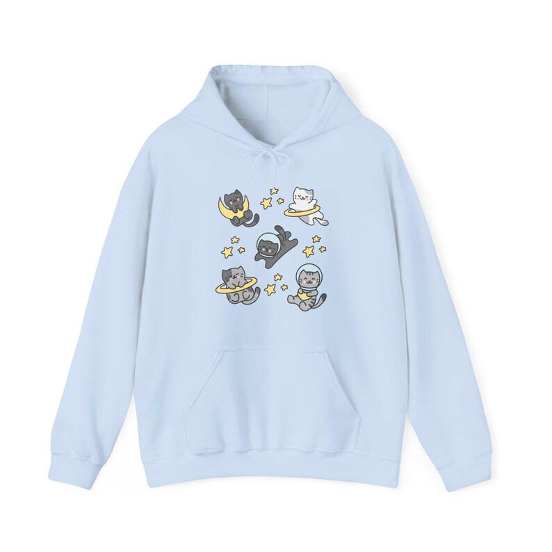 Peut inclure: Un sweat &agrave; capuche bleu clair orn&eacute; d'un motif ludique de chats de dessin anim&eacute; en combinaisons spatiales flottant dans l'espace. Les chats sont entour&eacute;s d'&eacute;toiles et de plan&egrave;tes. Le sweat &agrave; capuche a une poche avant et une capuche &agrave; cordon.