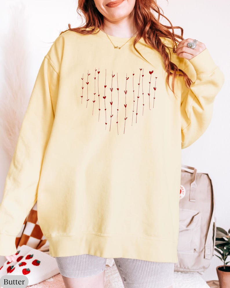 May include: A yellow sweatshirt with a red heart design made of small hearts and lines. The sweatshirt is oversized and has a crew neck.