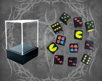 May include: A collection of black dice with various designs, including hearts, cherries, and Pac-Man characters. A clear display case with a black base is on the left. The dice are scattered on a gray background with a tribal design.
