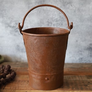 Könnte beinhalten: Ein rostiger Metalleimer mit Henkel. Der Eimer ist braun und hat einen abgenutzten, Vintage-Look.