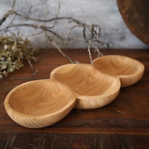 May include: A wooden serving tray with three separate bowls. The tray is made of light brown wood and has a natural finish.