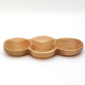May include: A wooden serving tray with three separate bowls. The tray is made of light brown wood and has a smooth, rounded shape.
