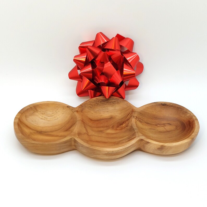 May include: A wooden serving tray with three separate bowls. The tray is made of natural wood and has a light brown color. The tray is perfect for serving snacks, dips, or appetizers.