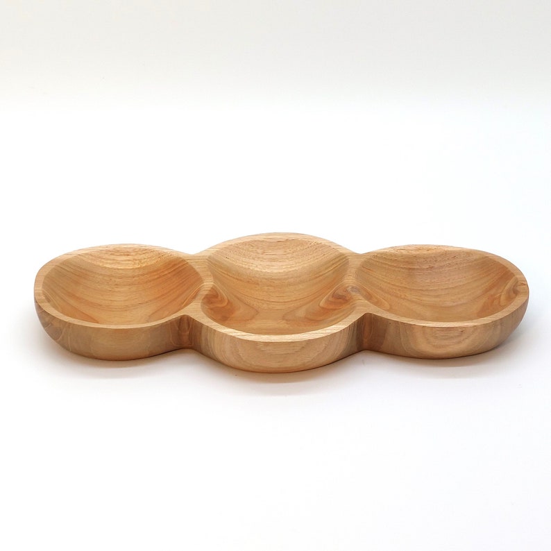 May include: A wooden serving tray with three separate bowls. The tray is made of light brown wood and has a smooth, rounded shape.
