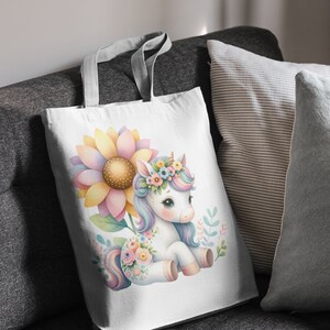 May include: A white tote bag with a colorful unicorn illustration. The unicorn is wearing a flower crown and is surrounded by flowers. The bag is made of canvas and has a white background.